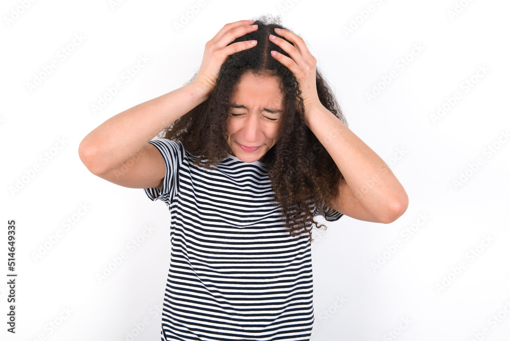 young beautiful girl with afro hairstyle wearing striped t-shirt over white wall holding head with hands, suffering from severe headache, pressing fingers to temples young beautiful girl with afro hairstyle wearing striped t-shirt over white wall holding head with hands, suffering from severe headache, pressing fingers to temples