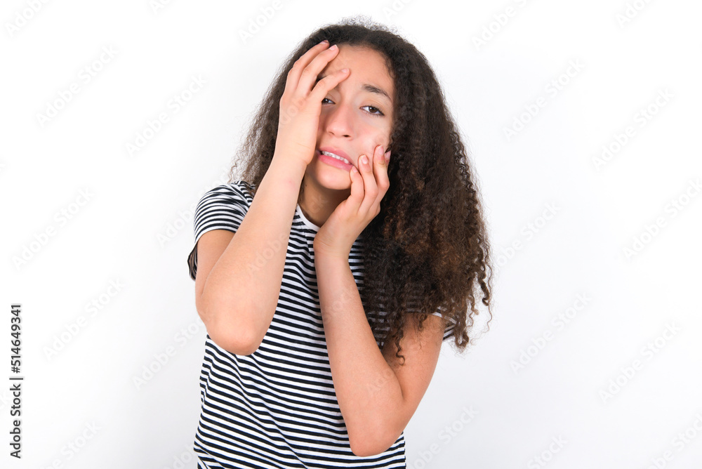 Young gloomy young beautiful girl with afro hairstyle wearing striped t-shirt over white wall, hiding face with hands pouting and crying, standing upset and depressed complaining about job problem. Young gloomy young beautiful girl with afro hairstyle wearing striped t-shirt over white wall, hiding face with hands pouting and crying, standing upset and depressed complaining about job problem.