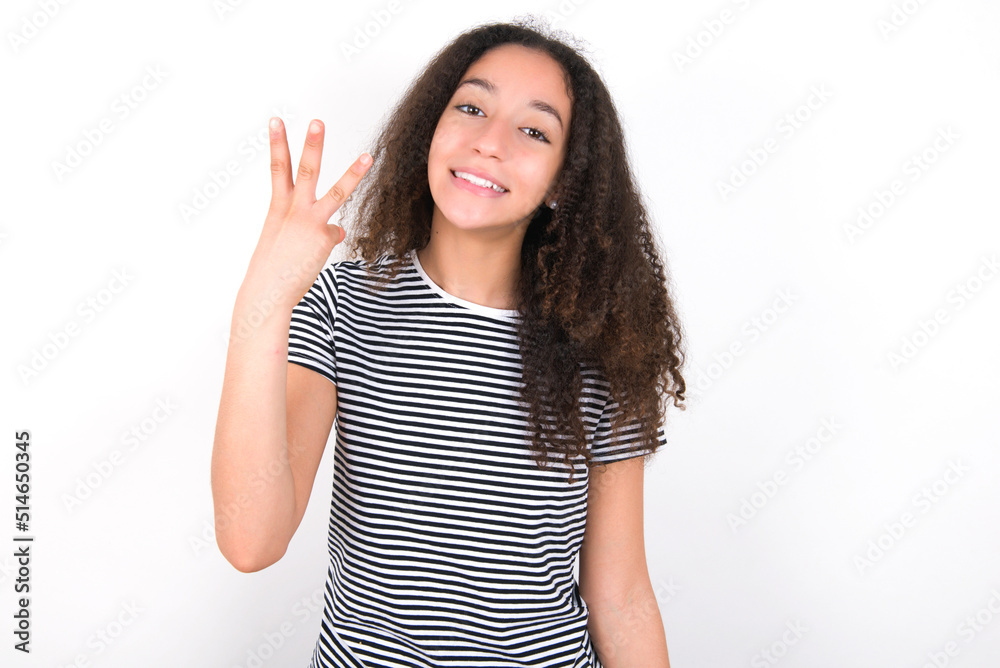 young beautiful girl with afro hairstyle wearing striped t-shirt over white wall smiling and looking friendly, showing number three or third with hand forward, counting down young beautiful girl with afro hairstyle wearing striped t-shirt over white wall smiling and looking friendly, showing number three or third with hand forward, counting down