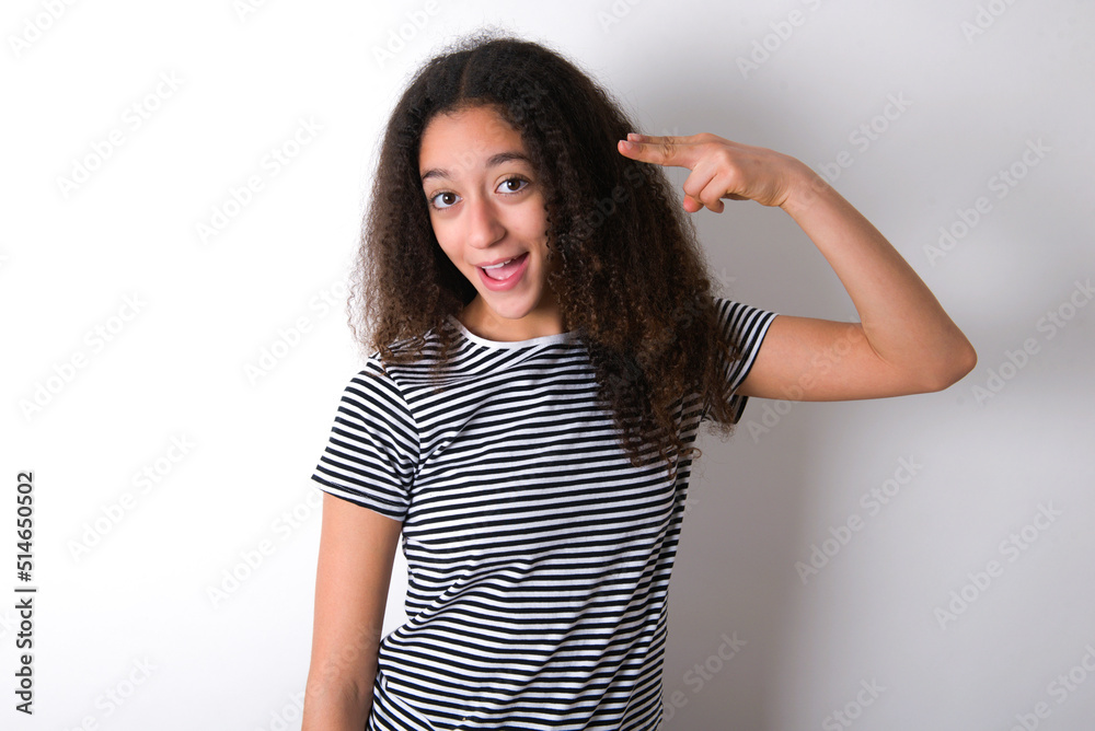 young beautiful girl with afro hairstyle wearing striped t-shirt over white wall foolishness around shoots in temple with fingers makes suicide gesture. Funny model makes finger gun pistol young beautiful girl with afro hairstyle wearing striped t-shirt over white wall foolishness around shoots in temple with fingers makes suicide gesture. Funny model makes finger gun pistol