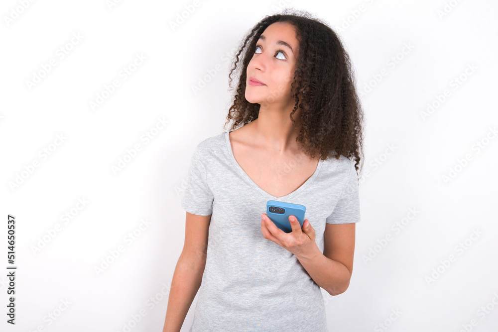 young beautiful girl with afro hairstyle wearing grey t-shirt over white wall holds mobile phone uses high speed internet and social networks has online communication. Modern technologies concept young beautiful girl with afro hairstyle wearing grey t-shirt over white wall holds mobile phone uses high speed internet and social networks has online communication. Modern technologies concept