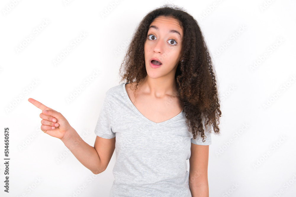 Emotive young beautiful girl with afro hairstyle wearing grey t-shirt keeps jaw dropped from shock demonstrates amazing promo points right on blank space demonstrates big shopping sale. Advertisement Emotive young beautiful girl with afro hairstyle wearing grey t-shirt keeps jaw dropped from shock demonstrates amazing promo points right on blank space demonstrates big shopping sale. Advertisement