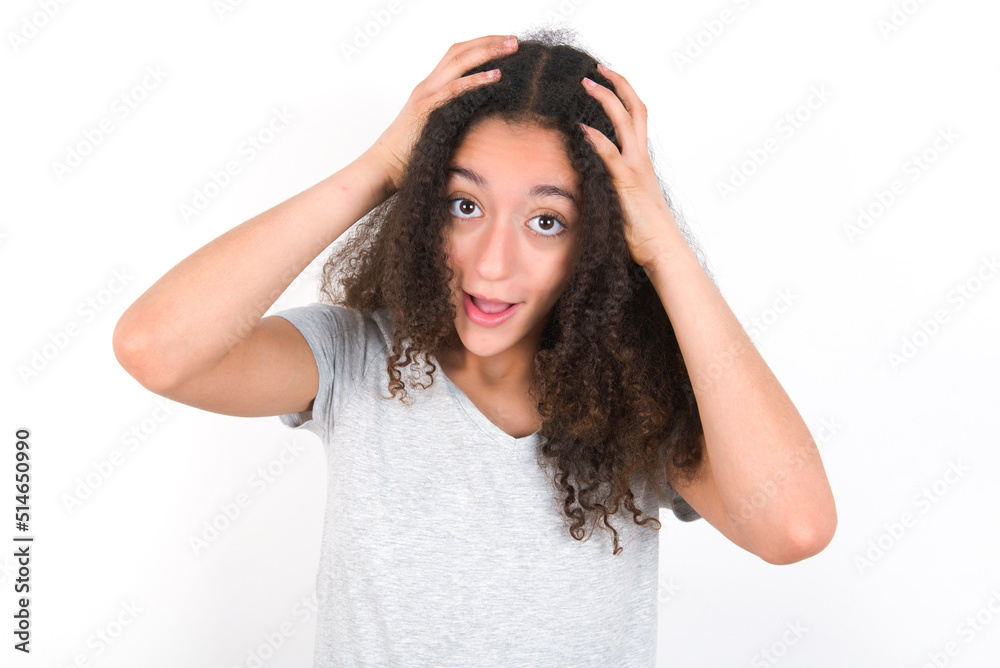 Cheerful overjoyed young beautiful girl with afro hairstyle wearing grey t-shirt over white wall reacts rising hands over head after receiving great news.