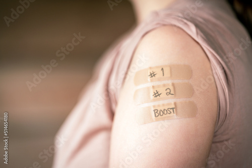 female with rolled up shirt sleeve to show the bandaids after the first two coronavirus vaccines and booster dose shot in the shoulder.