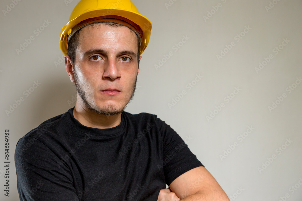 Worker with yellow safety hat for construction site work. Young white caucasian man with short hair, little beard and dark eyes.