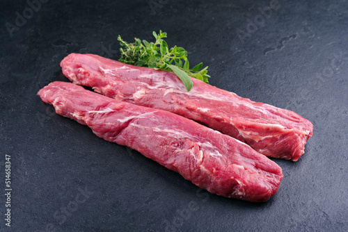 Traditional two raw duroc pork fillet pieces with herbs offered as close-up on a black board with copy space photo