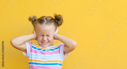 Unhappy little girl kid close eyes and cover ears hands being annoyed with noise wanting silence and calm atmosphere, isolated over yellow studio background