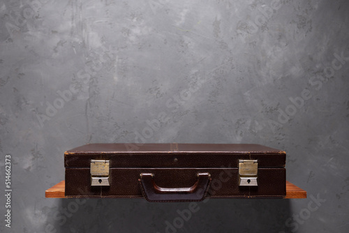 Old suitcase at shelf near wall. Shabby vintage suitcase