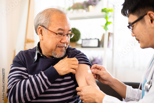 Safe vaccination for old people. Elder man in medical  getting flu or Covid-19 vaccine sitting on sofa at home. Asian Doctor or nurse giving flu or Covid-19 shot to senior.