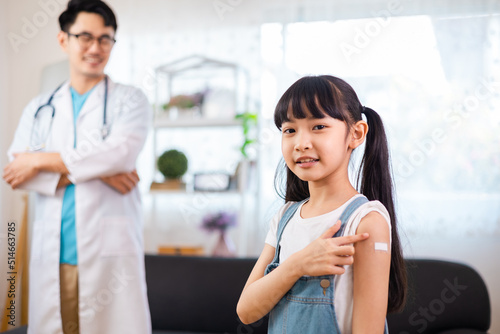 Young asian doctor wearing gloves and isolation is making a COVID-19 vaccination in the shoulder of child patient at home.