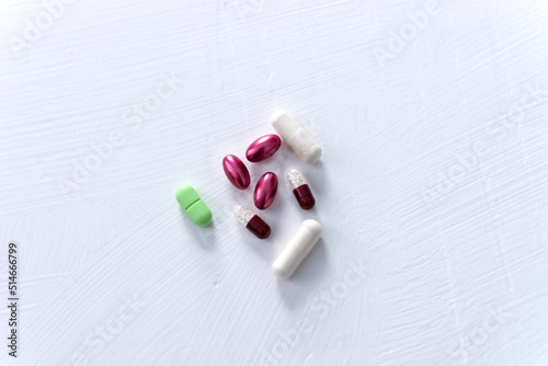 Pills and capsules in green, purple and brown on a white background.