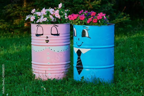 Metal tank painted faces in the garden. Flowerbeds with flowers from two iron barrels. Landscaping in the garden using recycled materials. Valentine's day concept. Symbol of male and female.