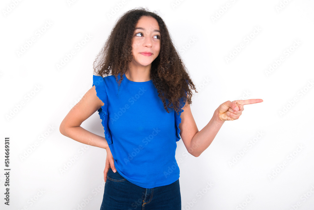 Obraz premium Smiling Teenager girl with afro hairstyle wearing blue T-shirt over white wall indicating finger empty space showing best low prices