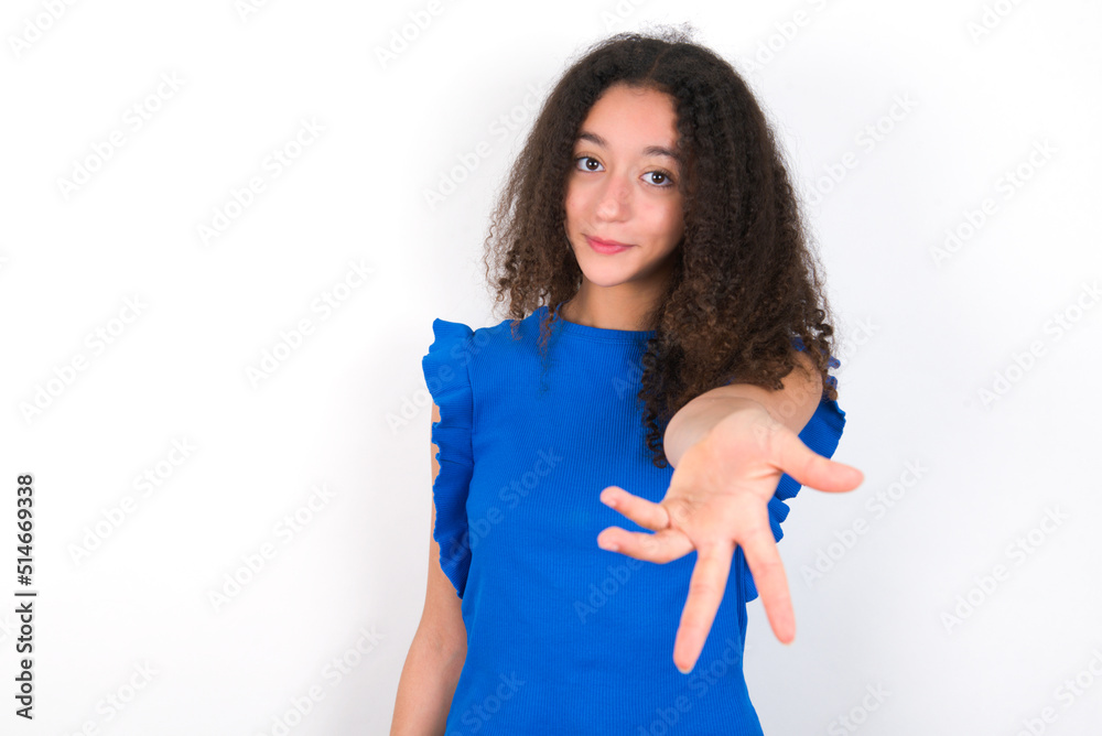 Teenager girl with afro hairstyle wearing blue T-shirt over white wall smiling cheerful offering palm hand giving assistance and acceptance. Teenager girl with afro hairstyle wearing blue T-shirt over white wall smiling cheerful offering palm hand giving assistance and acceptance.