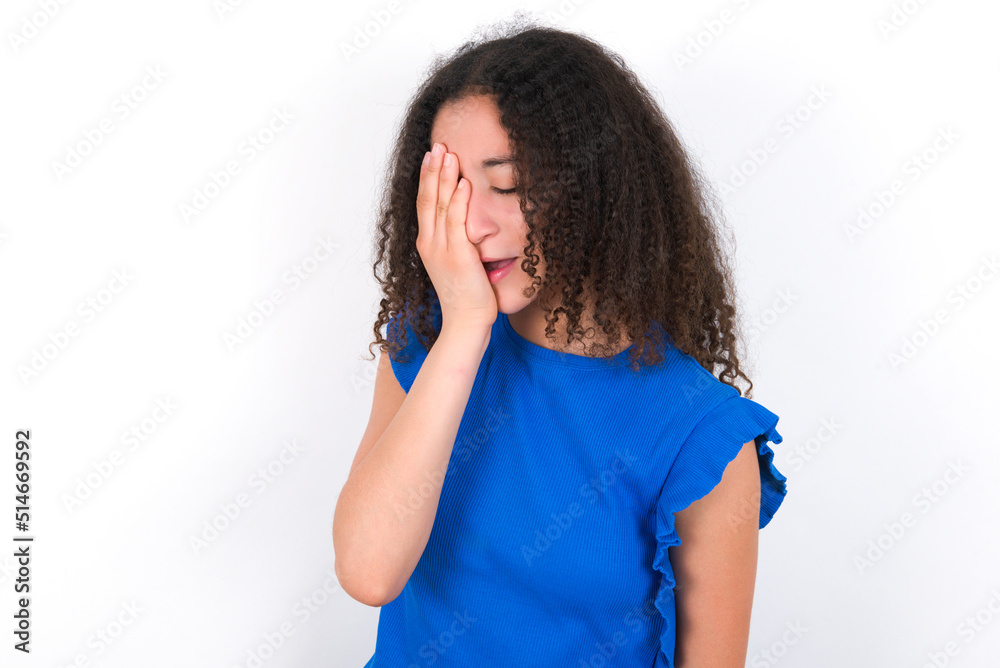 Teenager girl with afro hairstyle wearing blue T-shirt over white wall Yawning tired covering half face, eye and mouth with hand. Face hurts in pain. Teenager girl with afro hairstyle wearing blue T-shirt over white wall Yawning tired covering half face, eye and mouth with hand. Face hurts in pain.