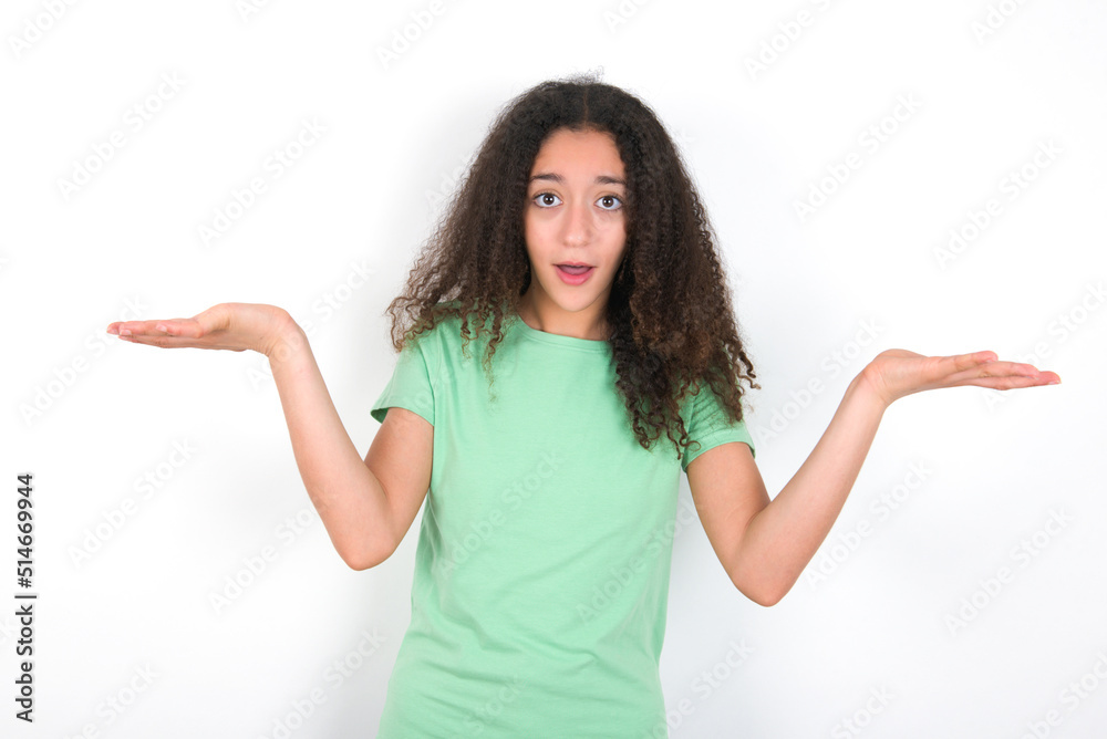 Surprised terrified Teenager girl with afro hairstyle wearing gr Gestures with uncertainty, stares at camera, puzzled as doesn't know answer on tricky question, People, body language, emotions concept Surprised terrified Teenager girl with afro hairstyle wearing gr Gestures with uncertainty, stares at camera, puzzled as doesn't know answer on tricky question, People, body language, emotions concept
