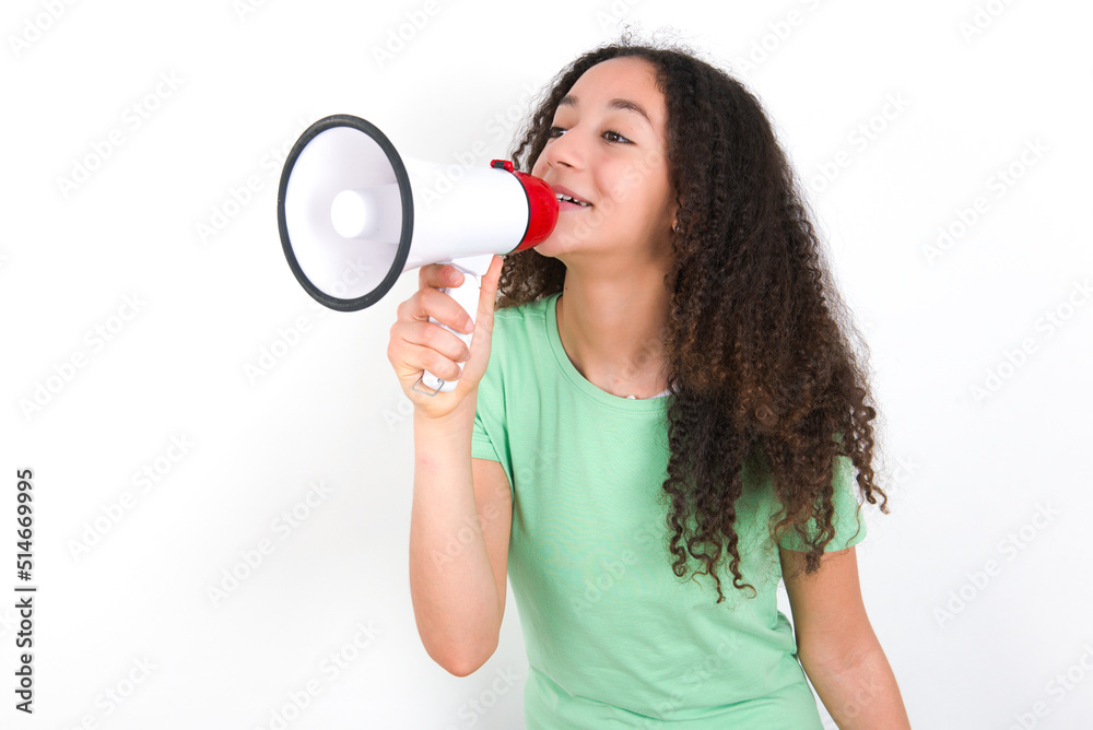 Teenager girl with afro hairstyle wearing green T-shirt over white wall Through Megaphone with Available Copy Space Teenager girl with afro hairstyle wearing green T-shirt over white wall Through Megaphone with Available Copy Space