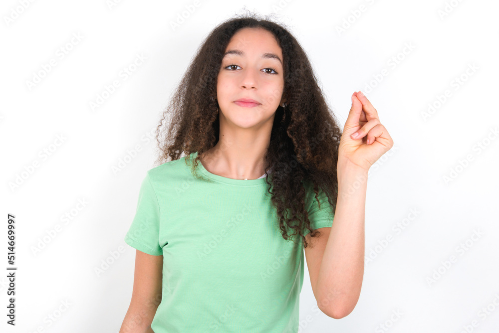 Teenager girl with afro hairstyle wearing green T-shirt over white wall pointing up with hand showing up seven fingers gesture in Chinese sign language QÄ«. Teenager girl with afro hairstyle wearing green T-shirt over white wall pointing up with hand showing up seven fingers gesture in Chinese sign language QÄ«.