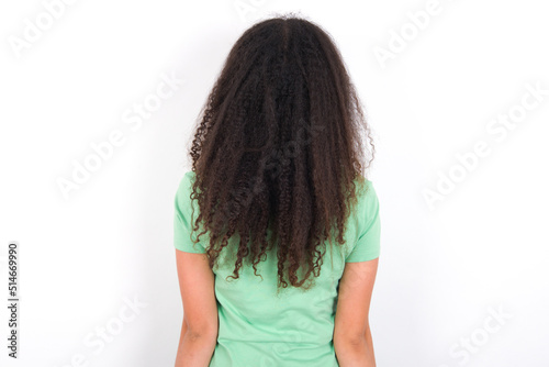 The back view of a Teenager girl with afro hairstyle wearing green T-shirt over white wall. Studio Shoot.