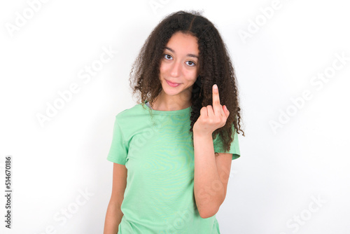 Teenager girl with afro hairstyle wearing green T-shirt over white wall shows middle finger bad sign asks not to bother. Provocation and rude attitude.