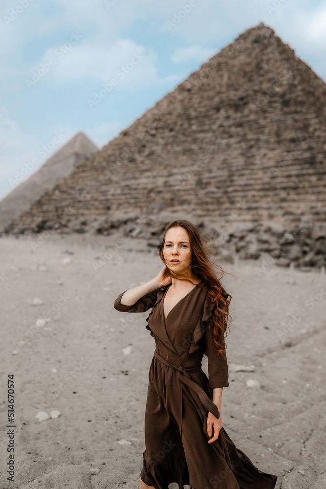 Φωτογραφία Young redhead tourist girl in brawn dress with a leather backpack standing on the sand in Egypt, Giza