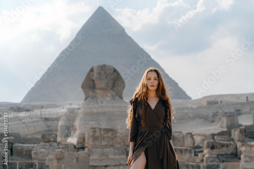 Young redhead woman standing in front of the Great Sphinx of Giza with the amazing Pyramid at the back. Valley of the Kings, Cairo, Egypt.