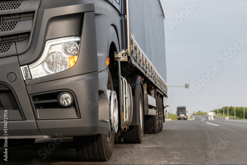 The concept of cargo transportation. Trucker's Day. A black truck is parked on the side of the highway. Front view of a heavy truck. Front headlight close-up. A place to copy.