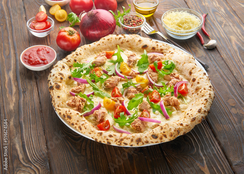 Tasty homemade seafood italian pizza with tuna fillet, onions, fresh herbs and mozzarella. Served with ingredients on a wooden table. Cooking ingredients, rustic background with a space for a text.