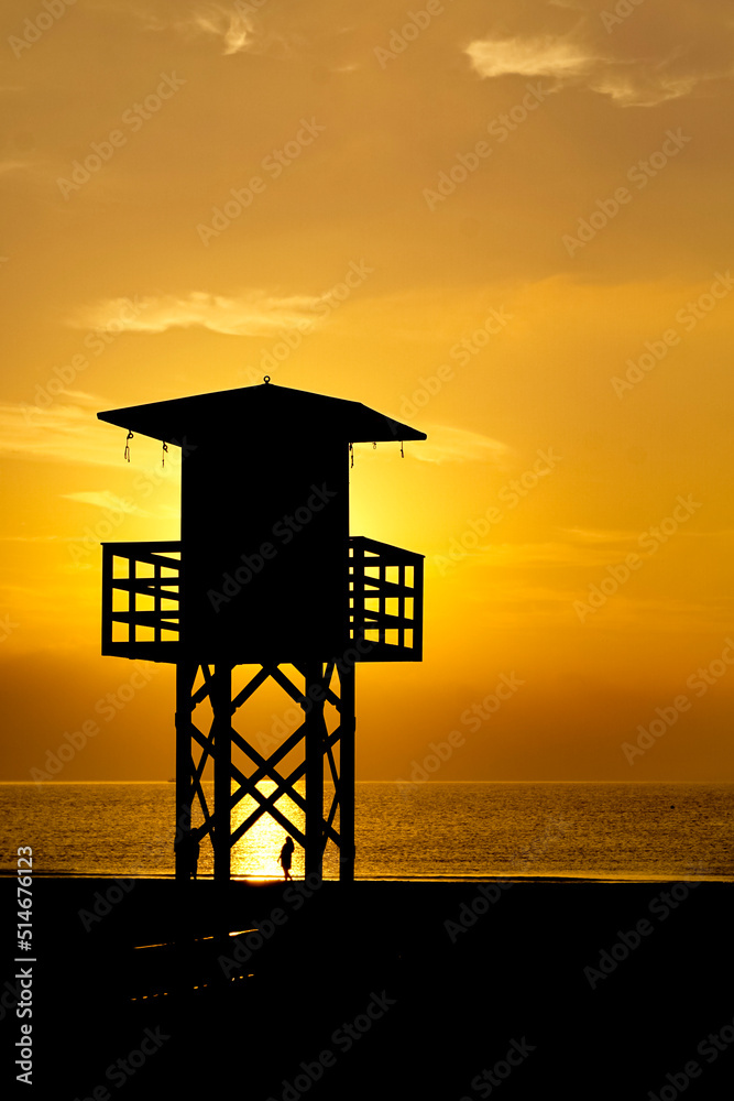 Backlit beach lifeguard huts at orange sunset