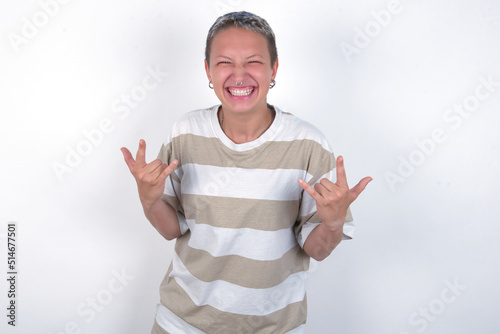 Born to rock this world. Joyful young woman with short hair wearing striped t-shirt over white background screaming out loud and showing with raised arms horns or rock gesture. photo