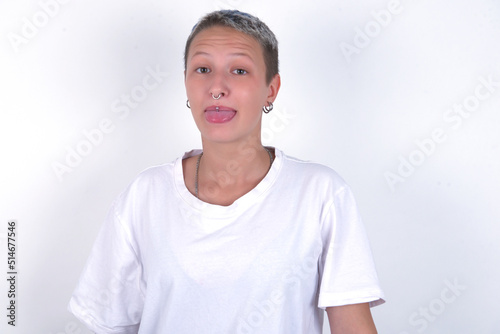 young woman with short hair wearing white t-shirt over white background with happy and funny face smiling and showing tongue.