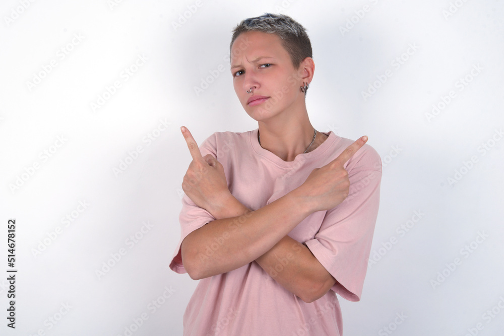 Serious young woman with short hair wearing pink t-shirt over white background crosses hands and points at different sides hesitates between two items. Hard decision concept Serious young woman with short hair wearing pink t-shirt over white background crosses hands and points at different sides hesitates between two items. Hard decision concept