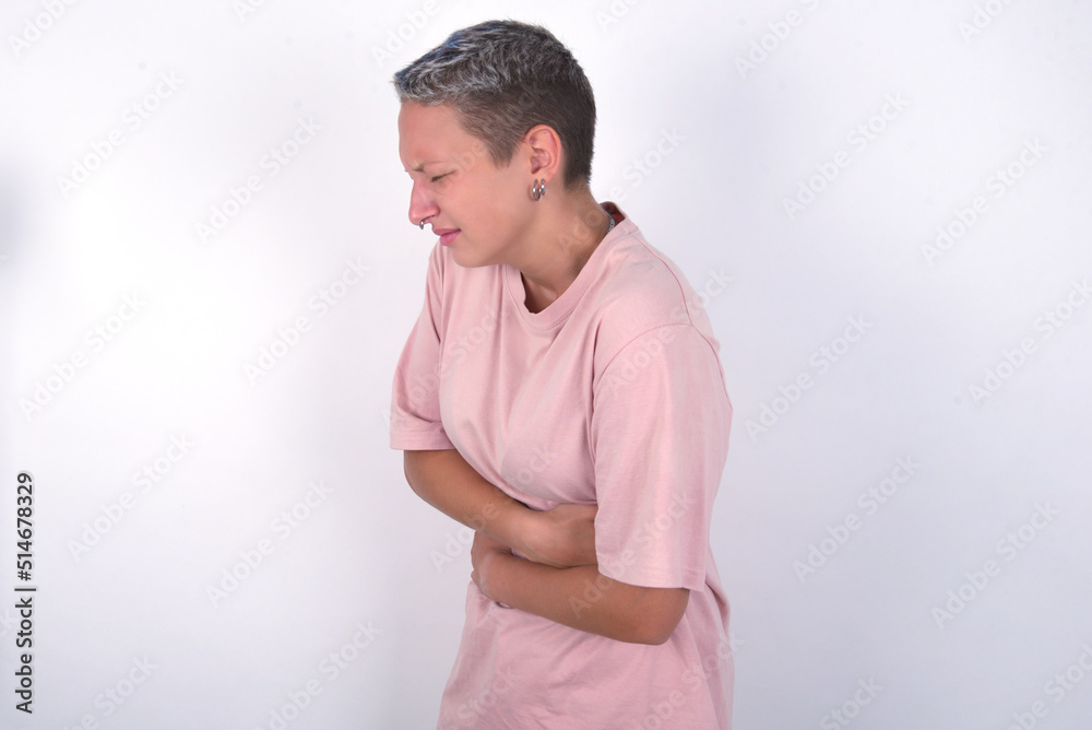 Obraz premium young woman with short hair wearing pink t-shirt over white background got stomachache