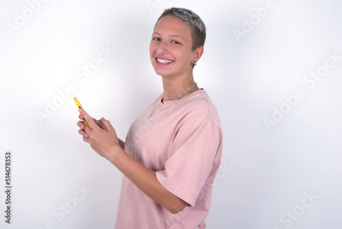 Rear view photo portrait of young woman with short hair wearing pink t-shirt over white background using smartphone smiling