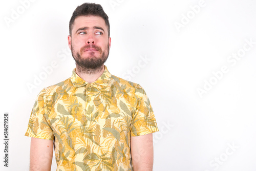 Wallpaper Mural Young caucasian man wearing Hawaiian t-shirt over white background  with thoughtful expression, looks away keeps hands down bitting his lip thinks about something pleasant. Torontodigital.ca
