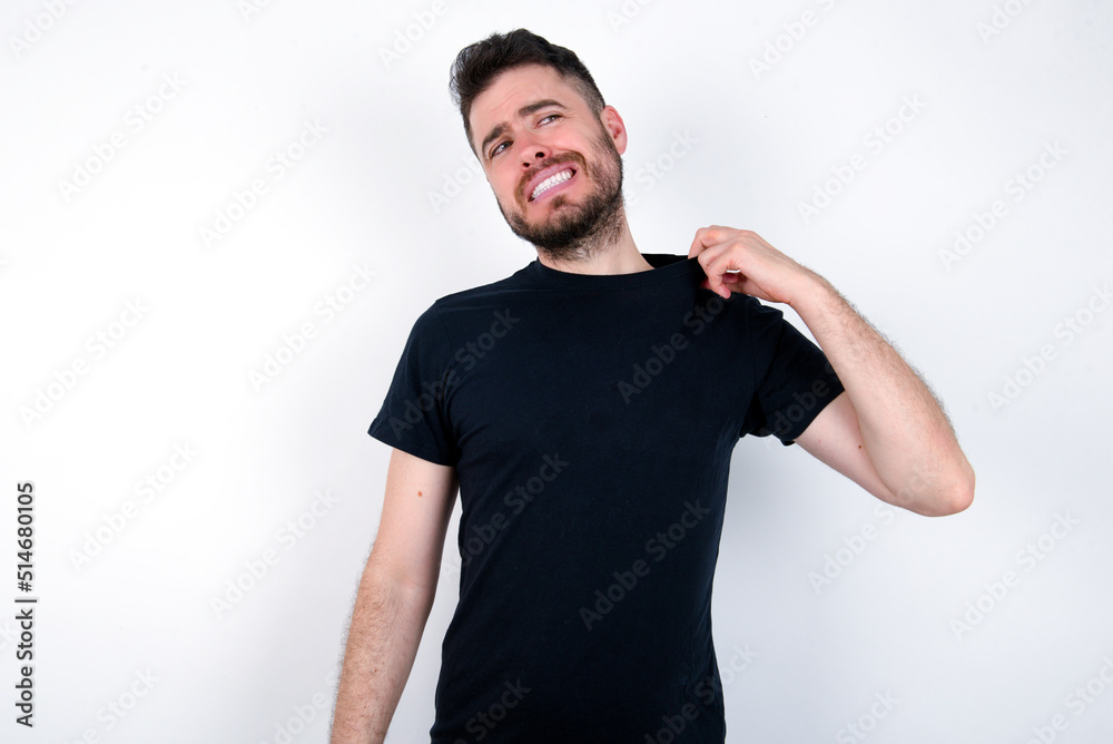 young caucasian bearded man wearing black t-shirt standing over white wall stressed, anxious, tired and frustrated, pulling shirt neck, looking frustrated with problem young caucasian bearded man wearing black t-shirt standing over white wall stressed, anxious, tired and frustrated, pulling shirt neck, looking frustrated with problem