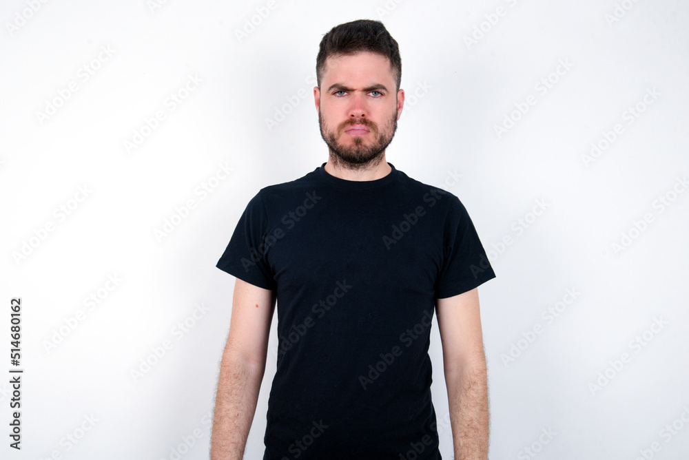 Fototapeta premium young caucasian bearded man wearing black t-shirt standing over white wall Pointing down with fingers showing advertisement, surprised face and open mouth