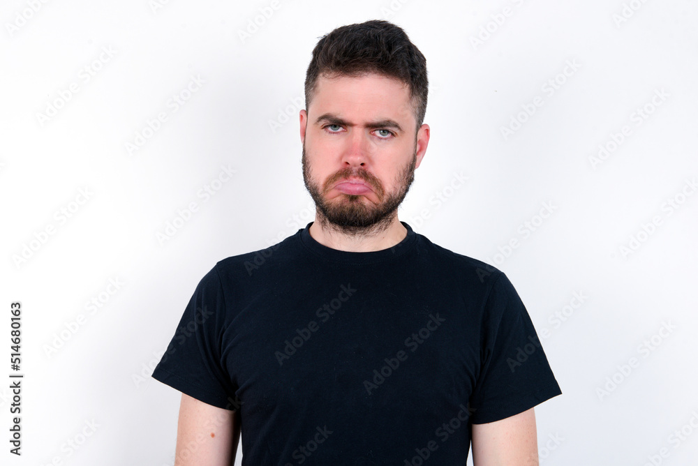 young caucasian bearded man wearing black t-shirt standing over white wall depressed and worry for distress, crying angry and afraid. Sad expression. young caucasian bearded man wearing black t-shirt standing over white wall depressed and worry for distress, crying angry and afraid. Sad expression.