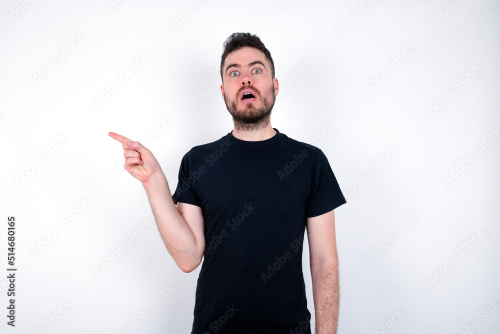 Emotive young caucasian bearded man wearing black t-shirt keeps jaw dropped from shock demonstrates amazing promo points right on blank space demonstrates big shopping sale. Advertisement Emotive young caucasian bearded man wearing black t-shirt keeps jaw dropped from shock demonstrates amazing promo points right on blank space demonstrates big shopping sale. Advertisement