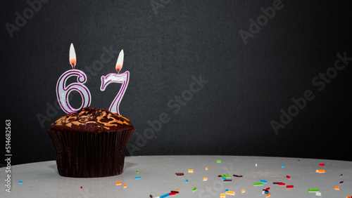  Muffin on black with a number from a candle number 67. Copy space, a pie on a black background, a card for congratulations on your birthday, anniversary.