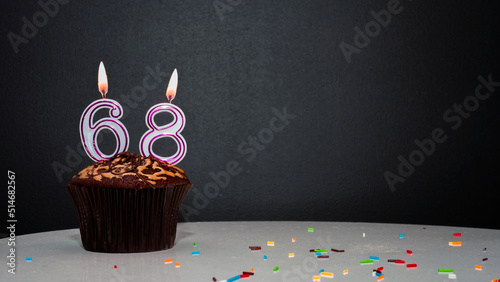 Muffin on black with a number from a candle number 68. Copy space, a pie on a black background, a card for congratulations on your birthday, anniversary.