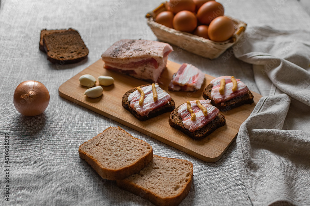 rustic natural food, on a linen tablecloth a wooden board, on it are ready-made sandwiches from black rye bread and lard with mustard and boiled eggs.