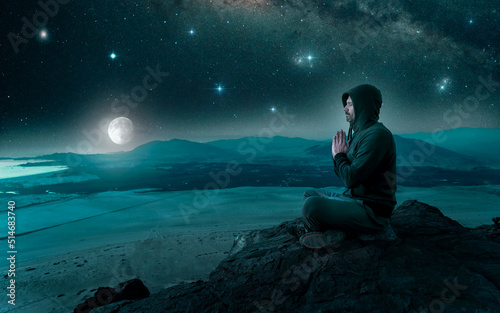 person sitting on the top of the mountain meditating or contemplating the starry night with full moon in the background.