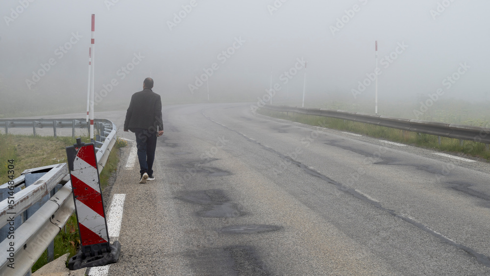 Man from behind walking on a mountain road, in the fog