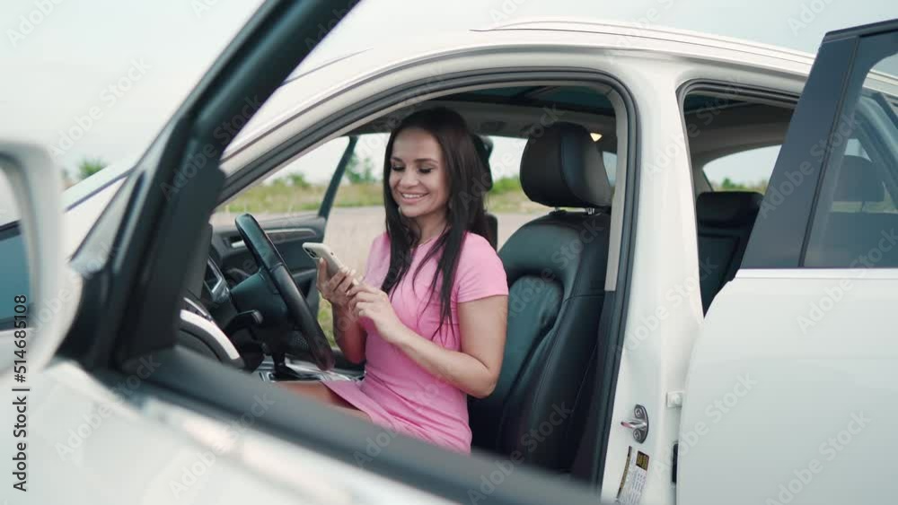 Young beautiful smiling girl holds the phone in his hands.Happy girl in a city with her new automobile holding.A young woman is sitting in the car. Young beautiful smiling girl holds the phone in his hands.Happy girl in a city with her new automobile holding.A young woman is sitting in the car.