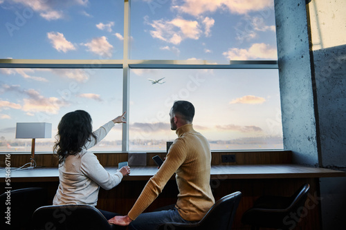 Принти на полотні Couple of passengers admire the plane taking off, sitting at panoramic windows i