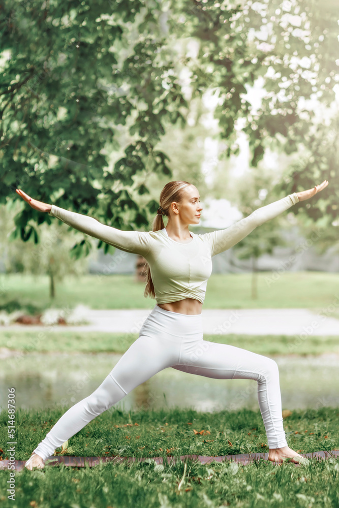 A young beautiful slender girl with long blonde hair does yoga in the summer in nature by the pond in the park. A young beautiful slender girl with long blonde hair does yoga in the summer in nature by the pond in the park.