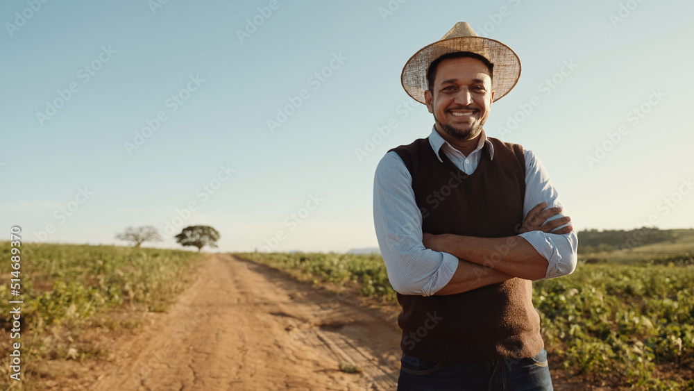 Portrait of young man with crossing hands in the casual shirt in the farm on the colorful sky background.
