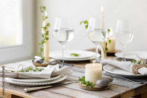 Rustic zero waste wedding decor with natural elements. Wooden table  candles  linen napkins  branches with green leaves. Eco-friendly decoration for the special dinner. Romantic and cozy place