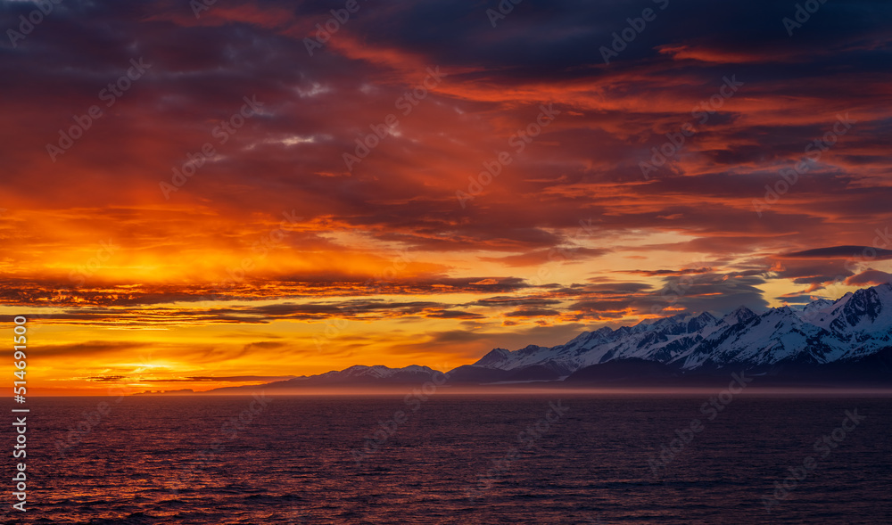Sun on the horizon by the mountains and Mount Fairweather by Glacier Bay National Park in Alaska